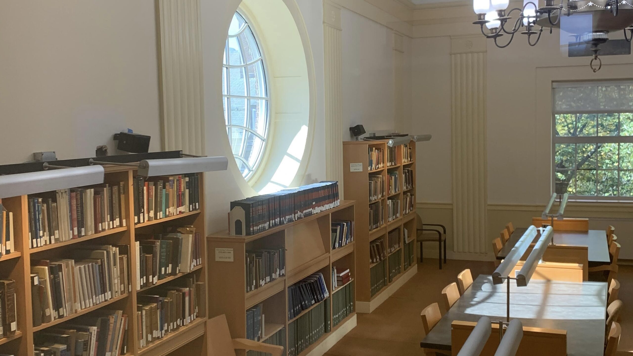 Image of library with book shelves, circular window, bathing a few tables in the room in the su